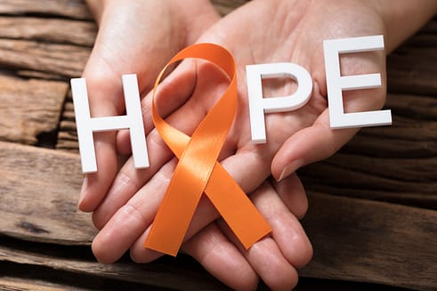 Multiple Sclerosis orange awareness ribbon in hands. The letters H P E and the loop in the ribbon spell HOPE. Research